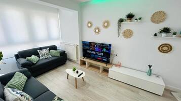 Ein modernes Wohnzimmer mit einem Flachbildfernseher, schwarzen Sofas, einem Couchtisch und dekorativer Wandkunst.