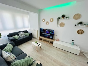 Una sala de estar moderna con un televisor de pantalla plana, sofás negros, una mesa de centro y arte decorativo en la pared.