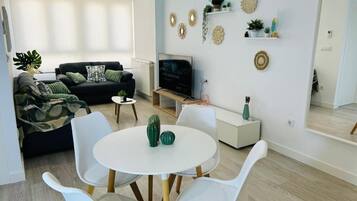 A modern living room with a sofa, a coffee table, and a TV. There are decorative wall pieces and a small plant on a shelf.