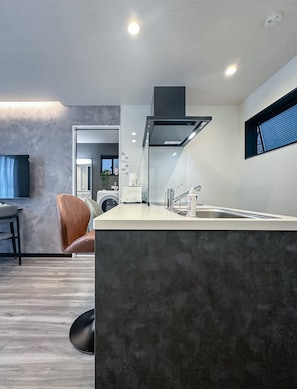 A modern kitchen with a built-in island, a washing machine, and a dining area with a leather chair. - HANASTAY MUKAI MIGIWA & SUZU (Osaka)