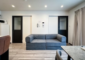 Un salon moderne avec un canapé gris, un plancher en bois, une petite table et un four à micro-ondes sur le côté gauche.