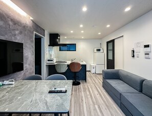 A compact living space with a kitchenette, a seating area, and a flat-screen TV. - HANASTAY MUKAI MIGIWA & SUZU (Osaka)
