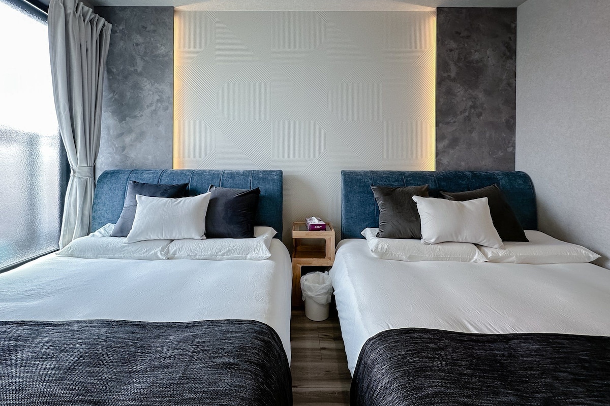 A hotel room with two beds, a nightstand, and a window with curtains.