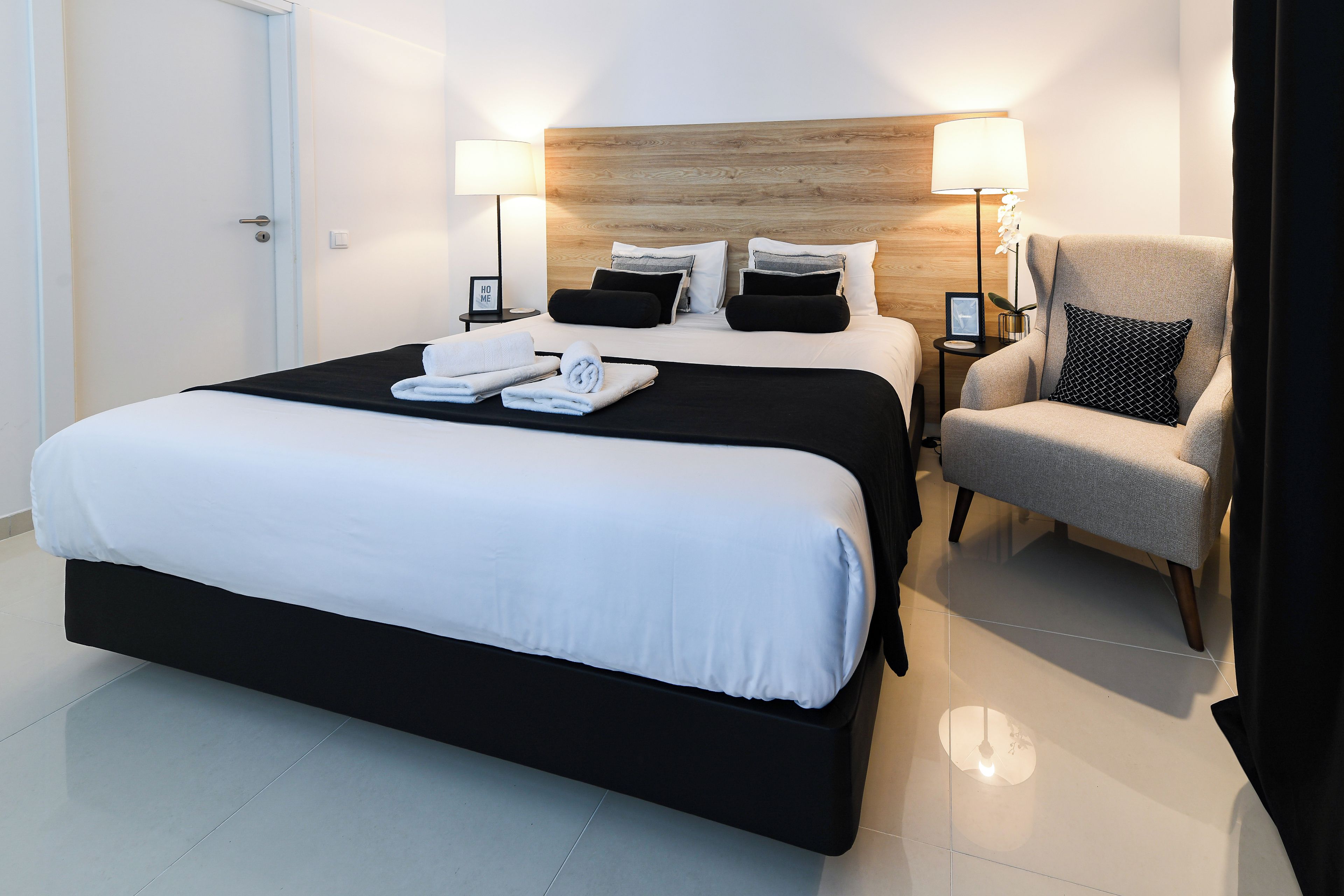 Ein Hotelzimmer mit einem großen Bett, zwei Nachttischen, einem Sessel und einem hölzernen Kopfteil.