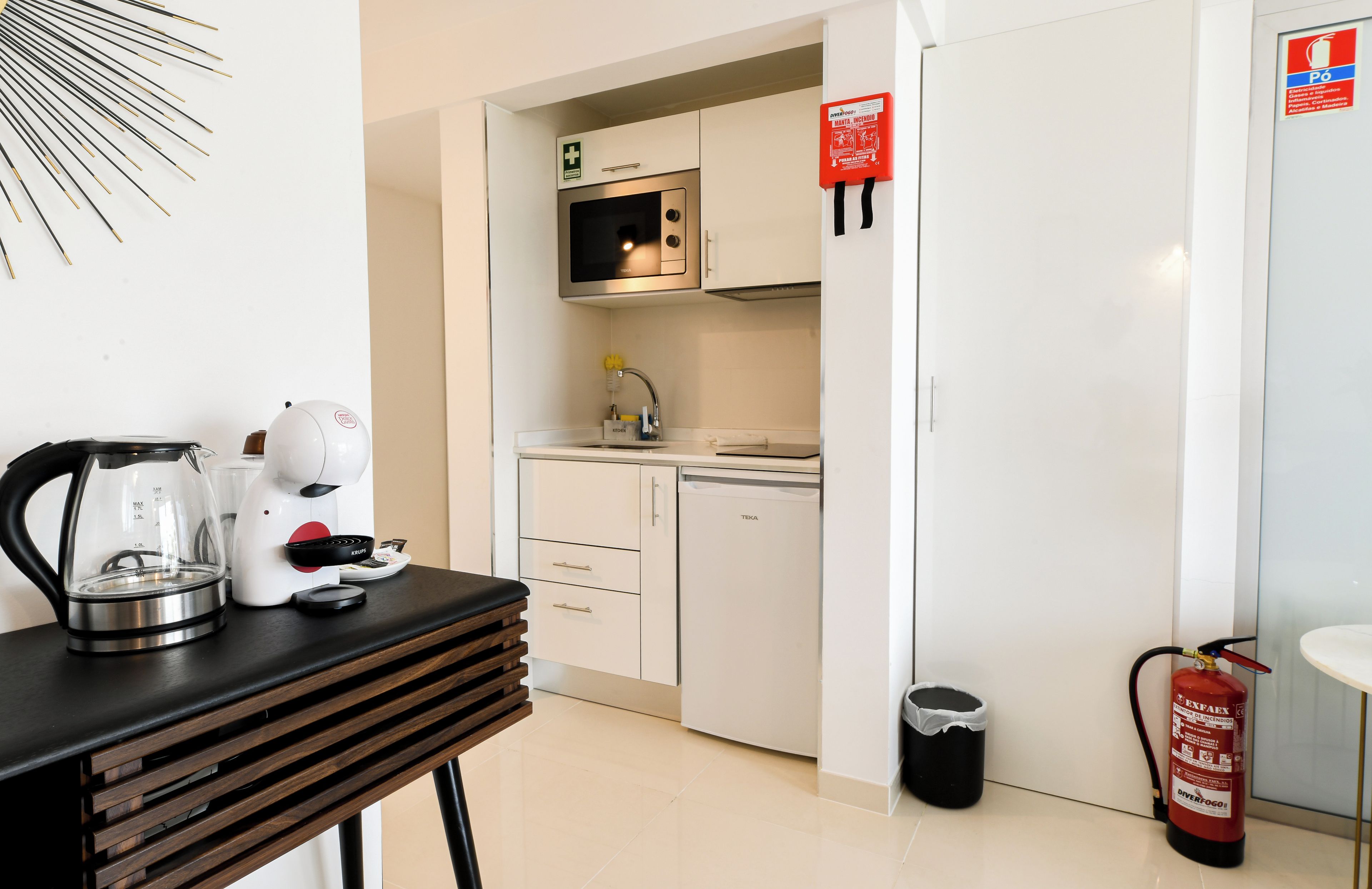 A kitchenette with a microwave, stove, and sink. There is a fire extinguisher and a trash can visible.