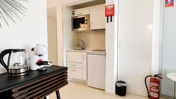 A kitchenette with a microwave, stove, and sink. There is a fire extinguisher and a trash can visible.