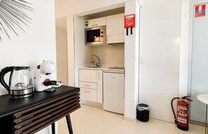Une petite cuisine équipée d’un four à micro-ondes, d’une cuisinière et d’un évier. On peut voir un extincteur et une poubelle.