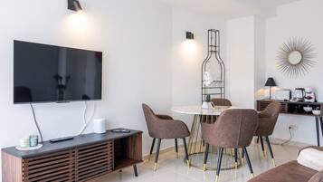 A modern living room with a flat-screen TV, a round dining table with chairs, a sofa, and a coffee table.