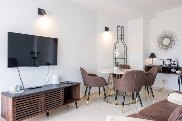 Un salon moderne avec un téléviseur à écran plat, une table de salle à manger ronde entourée de chaises, un canapé et une table basse.