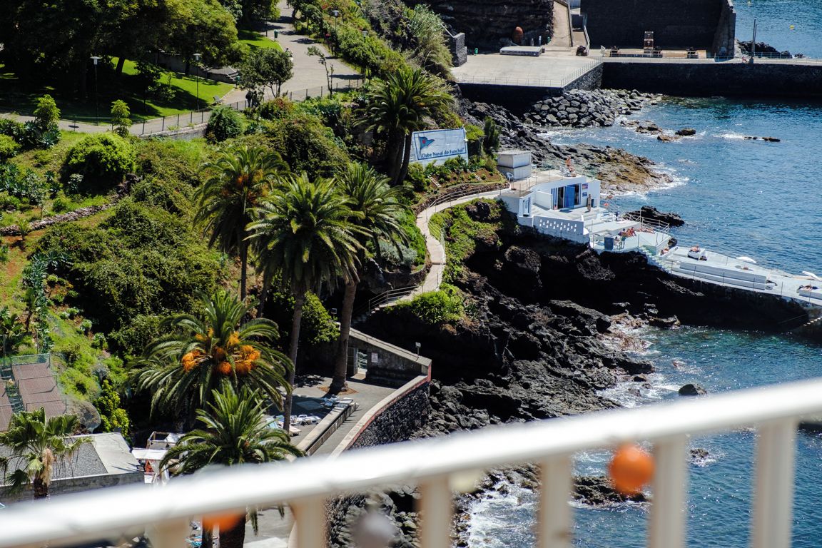 Ein Küstenhotel mit felsiger Uferlinie, Palmen und freiem Blick auf das Meer.