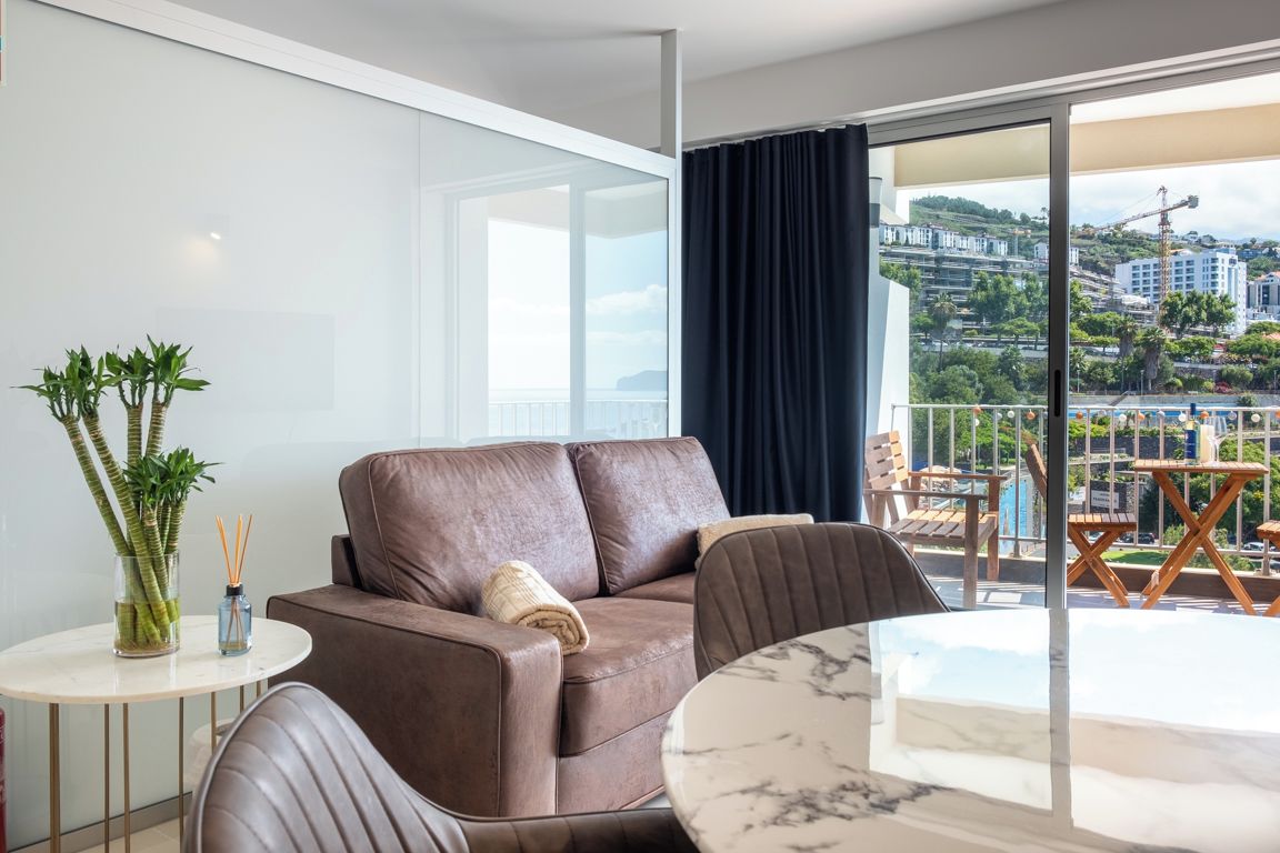 A modern living room with a brown leather sofa, a round marble table, and a view of a cityscape through large windows.