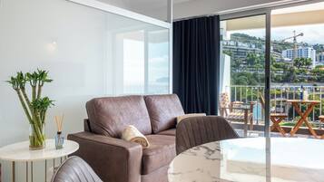 A modern living room with a brown leather sofa, a round marble table, and a view of a cityscape through large windows.