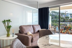 A modern living room with a brown leather sofa, a round marble table, and a view of a cityscape through large windows. - Atlantic Calling - first Line with stunning Sea View and own parking space (Funchal)