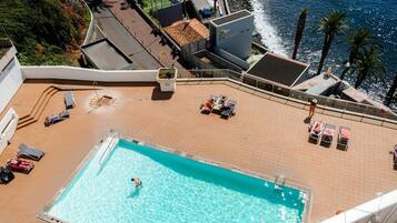 Une piscine sur le toit offrant une vue sur l’océan, entourée de chaises longues et de parasols.