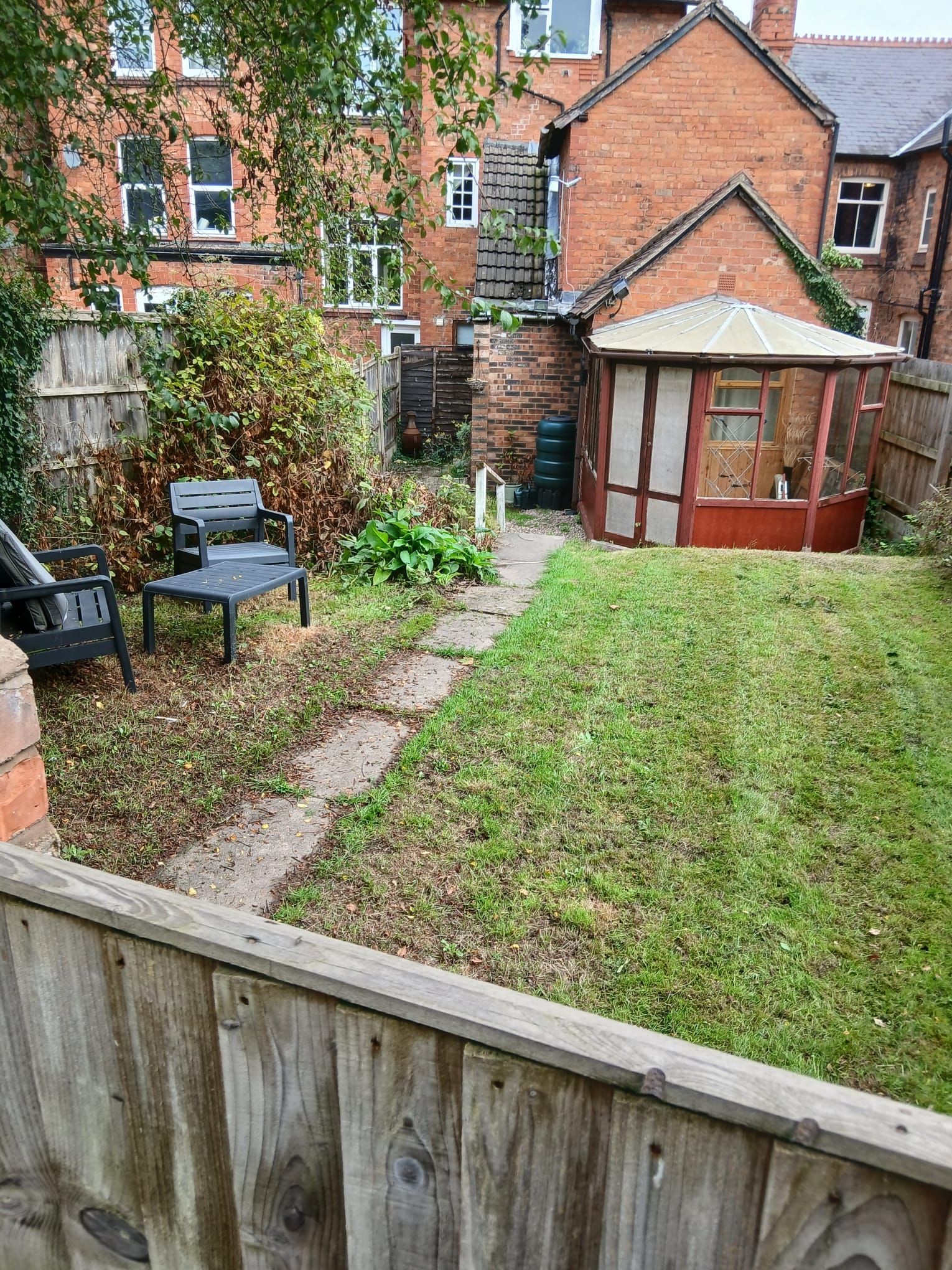 A backyard with a wooden fence, a small garden, and a conservatory.