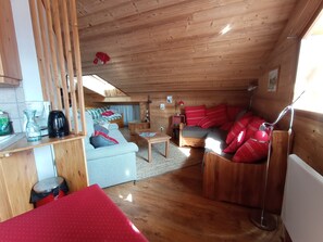 A cozy cabin interior with a wooden ceiling, a sofa, a dining table, and a red chair. - Duplex apartment at the base of the slopes, sleeps 6, 50 m²—Les Saisies—Les Contamines-Montjoie (Hauteluce)
