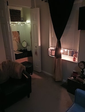 Une pièce comprenant un lit, une chaise, une fenêtre avec des rideaux, une table de chevet et une horloge murale.