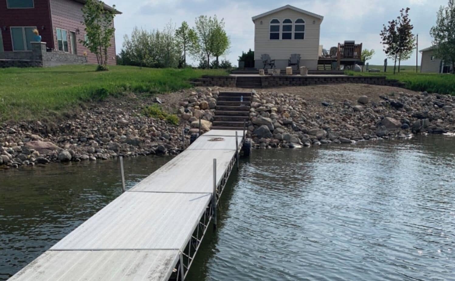 A wooden dock extending into a body of water, with a stone staircase leading up to a building with a gabled roof.