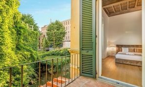 Un balcon donnant sur le paysage urbain, un lit avec une tête de lit en bois et une petite table avec une lampe.