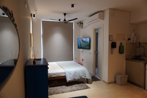 Ein Schlafzimmer mit einem Bett, einem Deckenventilator, einem Fernseher und einer Küchenzeile.