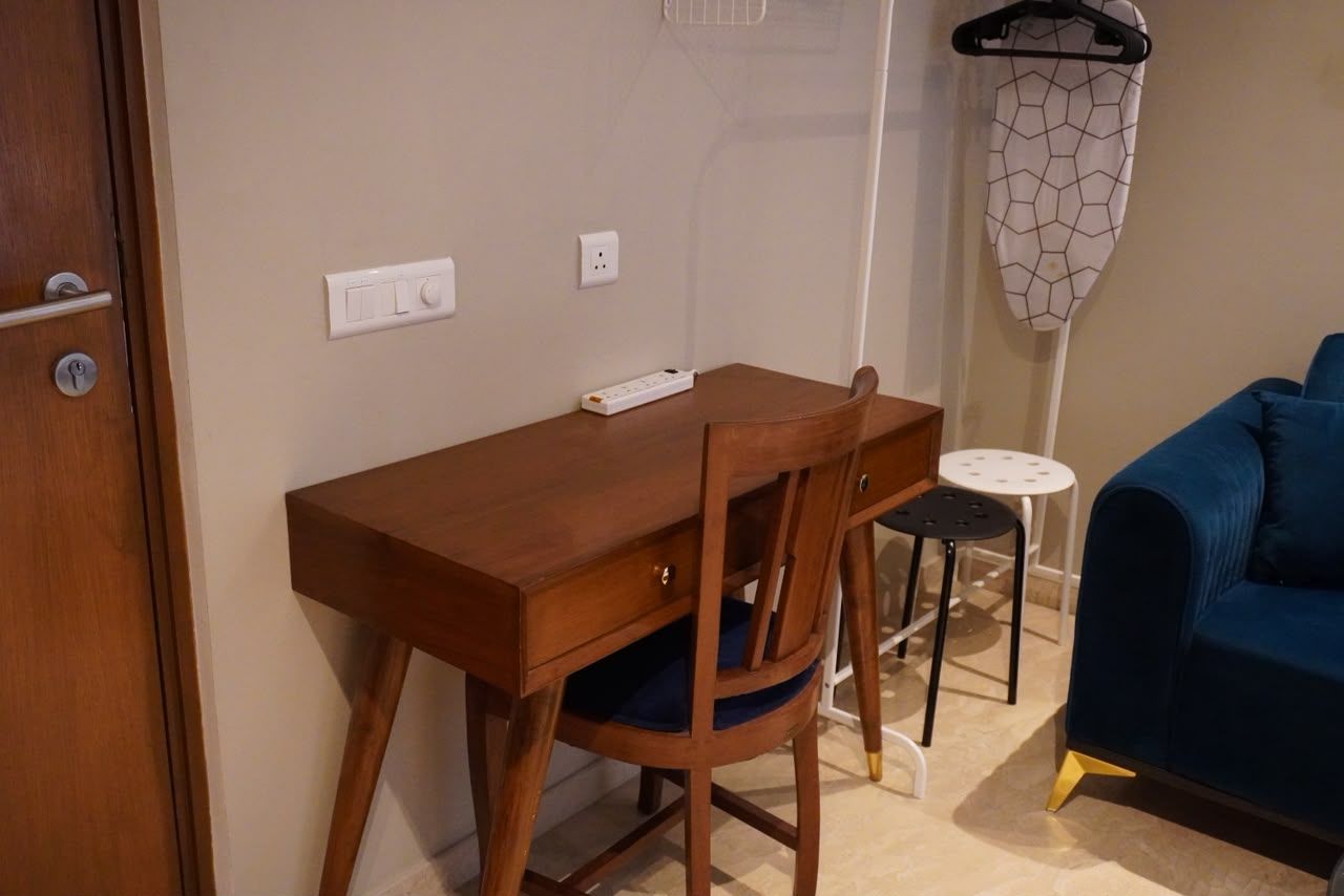 A wooden desk with a chair, a power strip, a small white table, and a blue sofa.