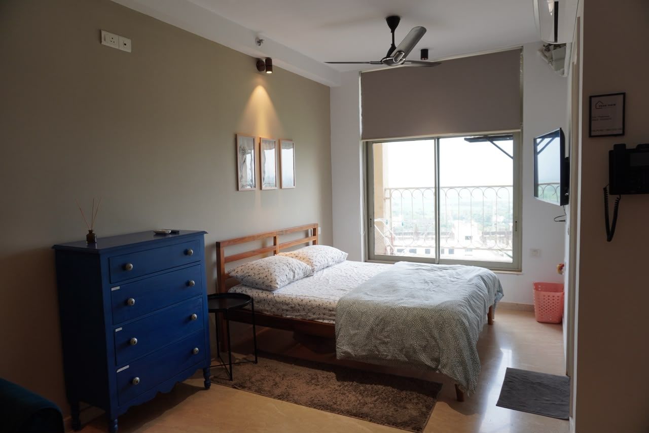 A bedroom with a bed, a dresser, a ceiling fan, a window with a view, and a wall-mounted TV.