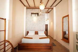 A bedroom with a wooden bed, a nightstand, a mirror, and a ceiling light fixture. - Mini Beach Villa - Hikkaduwa (Hikkaduwa)