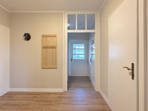 Een gang met een houten vloer, een deur met een raam en een ventilatierooster aan de muur.