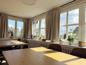 Een kamer met grote ramen, een lange tafel en stoelen.
