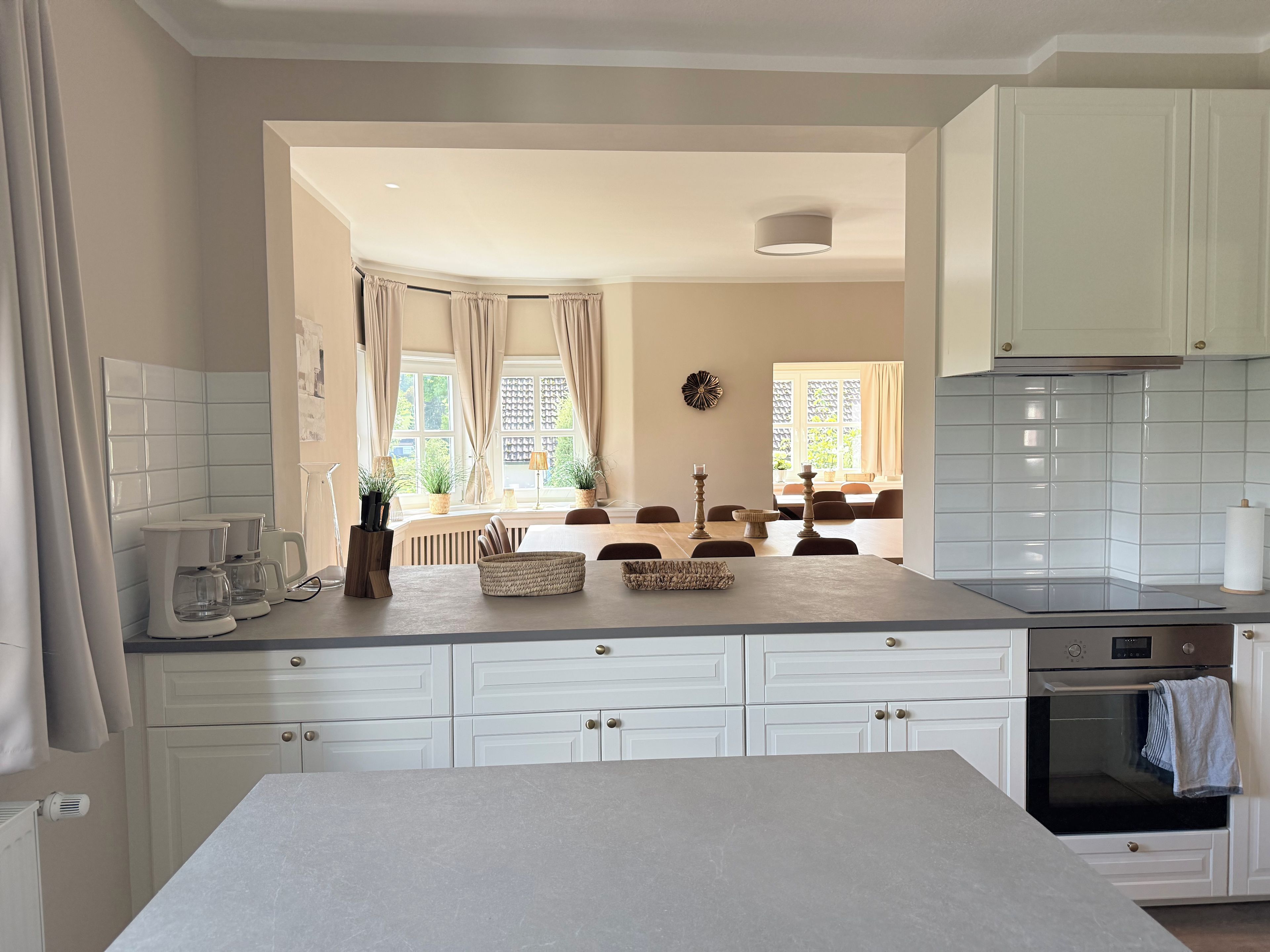 A modern kitchen with white cabinetry, a central island, and a dining area with a view of the garden.