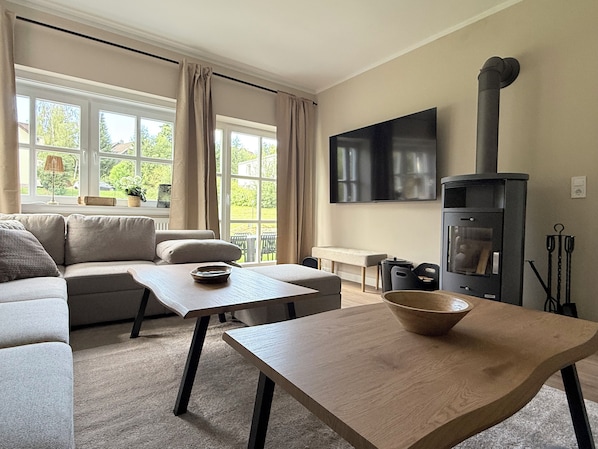 Een moderne woonkamer met een bank, een salontafel, een televisie en een houtkachel.