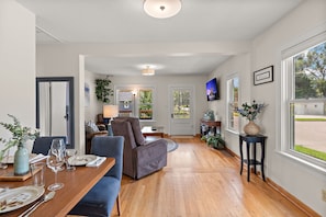 A spacious living area with a dining table set for six, a comfortable sofa, and a television mounted on the wall.