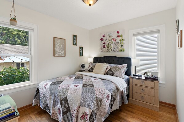 A bedroom with a bed, bedside table, dresser, and a window with blinds.