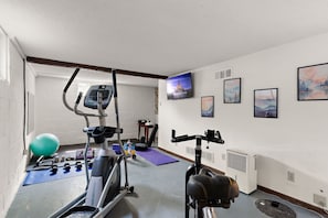 A gym with exercise equipment, a large exercise ball, and a wall-mounted TV displaying a Disney movie.