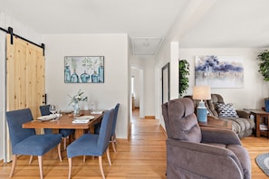 A modern living room with a sofa, a dining area with a wooden table and chairs, and a hallway leading to another room.