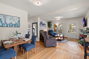 A spacious living room with a dining area, a large painting, and a television mounted on the wall.