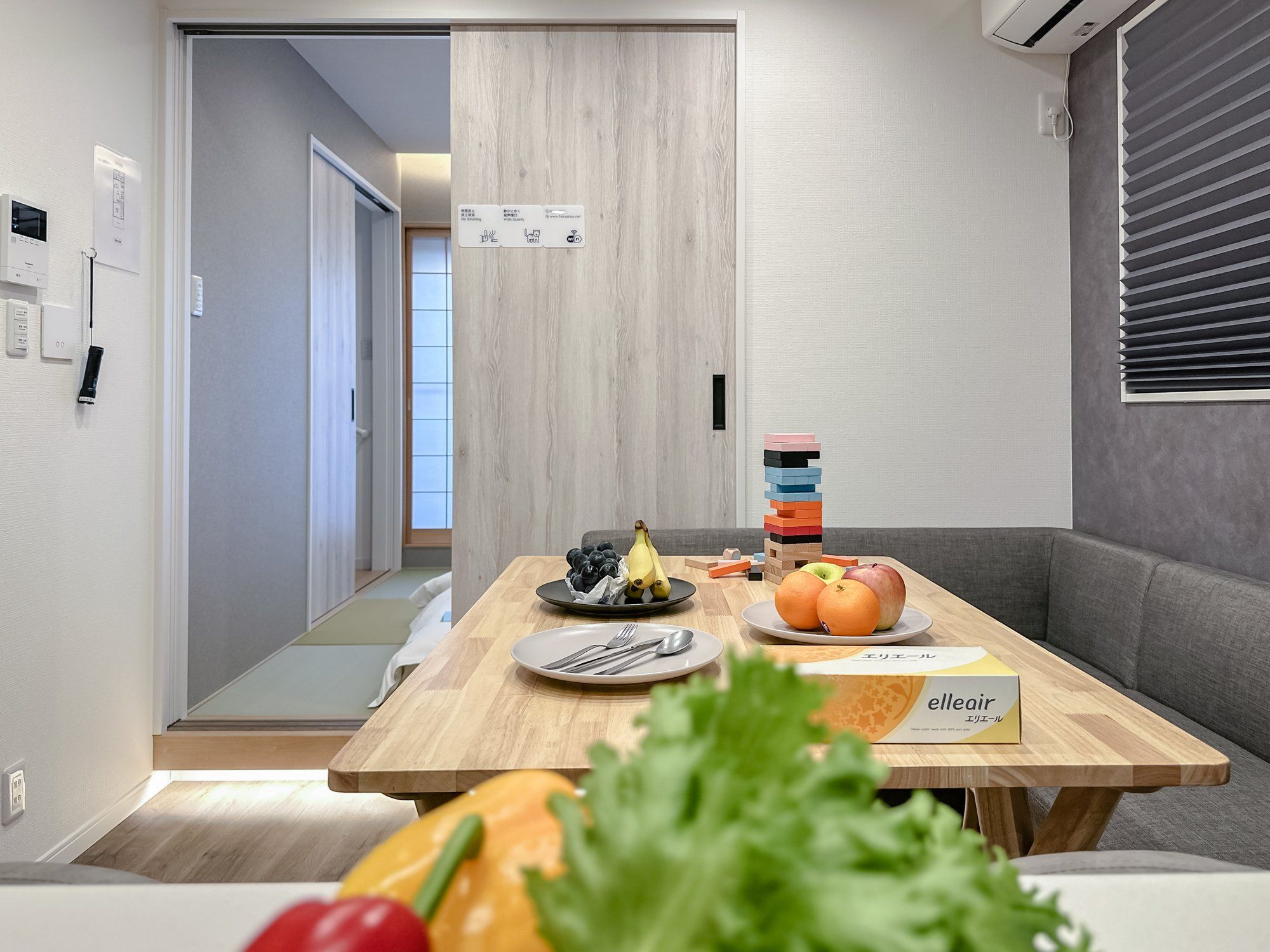 A modern dining area with a wooden table, plates, cutlery, and a fruit bowl.