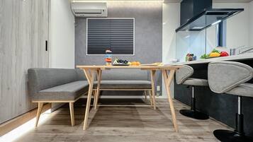 A compact kitchen with a dining area, featuring a built-in stove, a window with blinds, and a small table with a bench.
