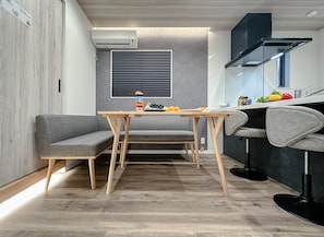 Cozinha compacta com área de refeições, com fogão embutido, janela com persianas e pequena mesa com banqueta.