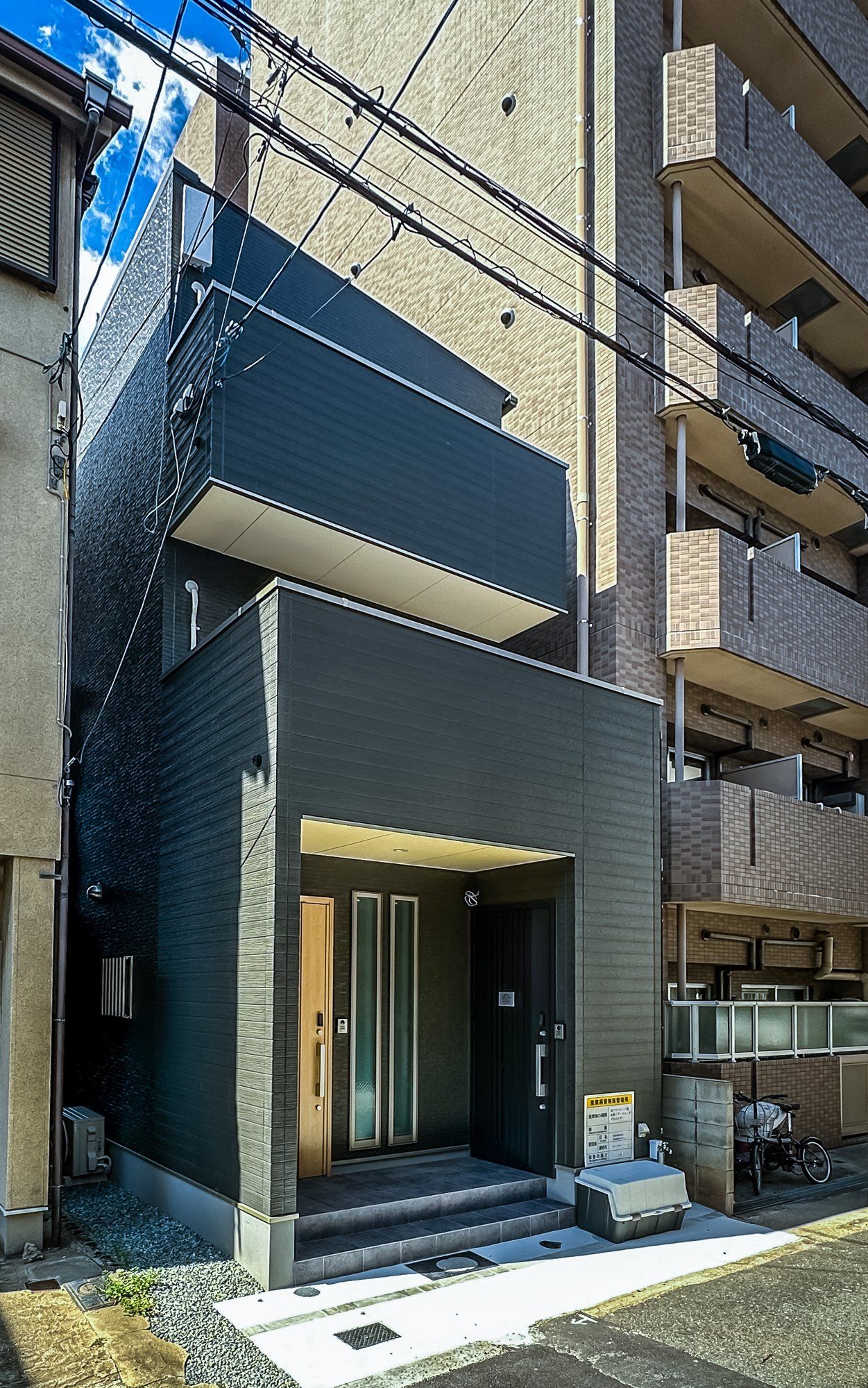 A modern building with a flat roof, a balcony, and a ground-level entrance with steps.