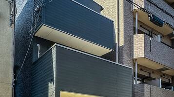 A modern building with a flat roof, a balcony, and a ground-level entrance with steps.