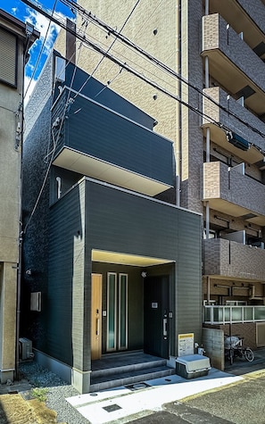 Um edifício moderno com telhado plano, varanda e entrada no nível da rua com degraus.