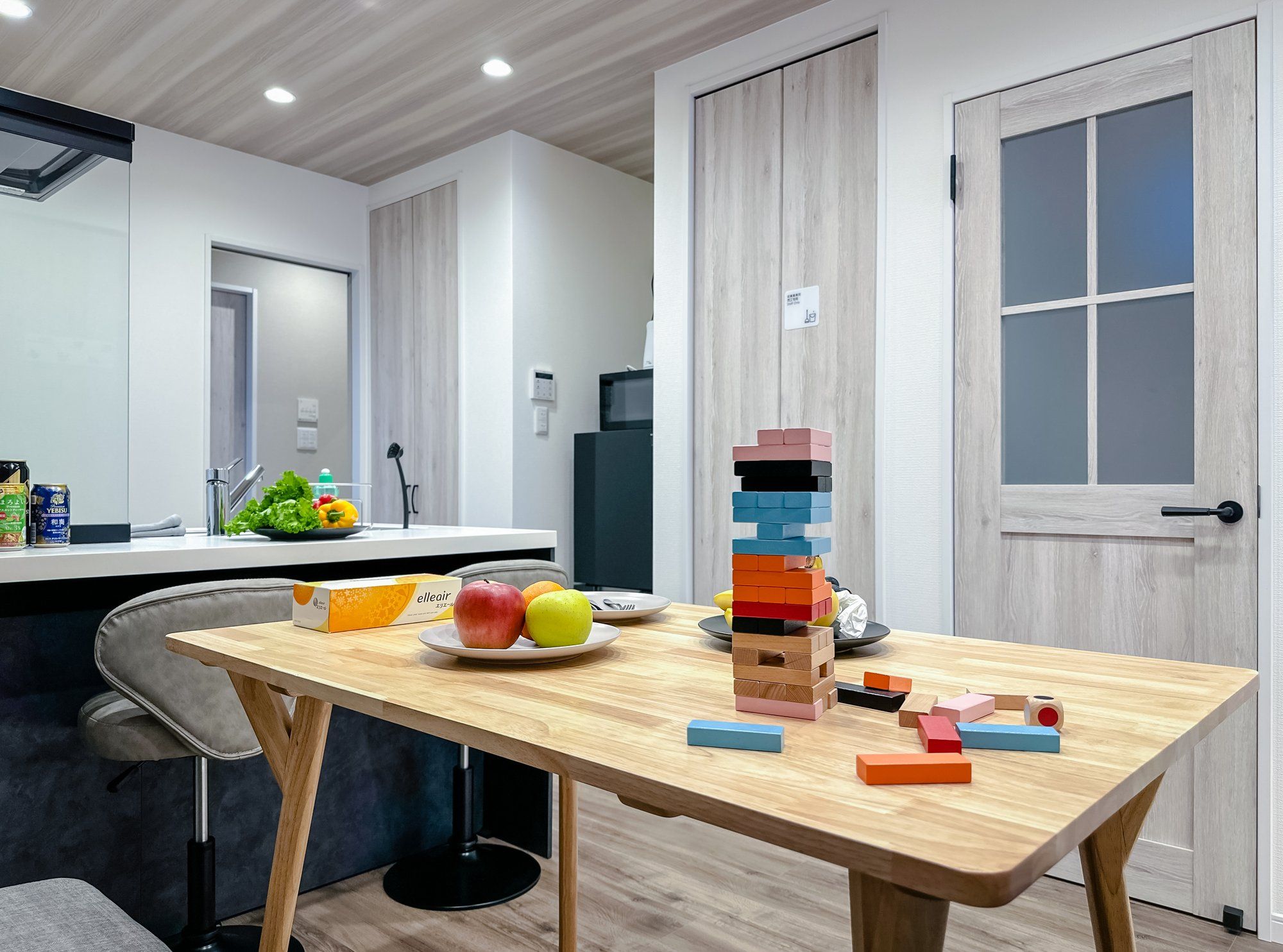 A modern kitchen with a wooden table, fruits, and a stack of colorful blocks.