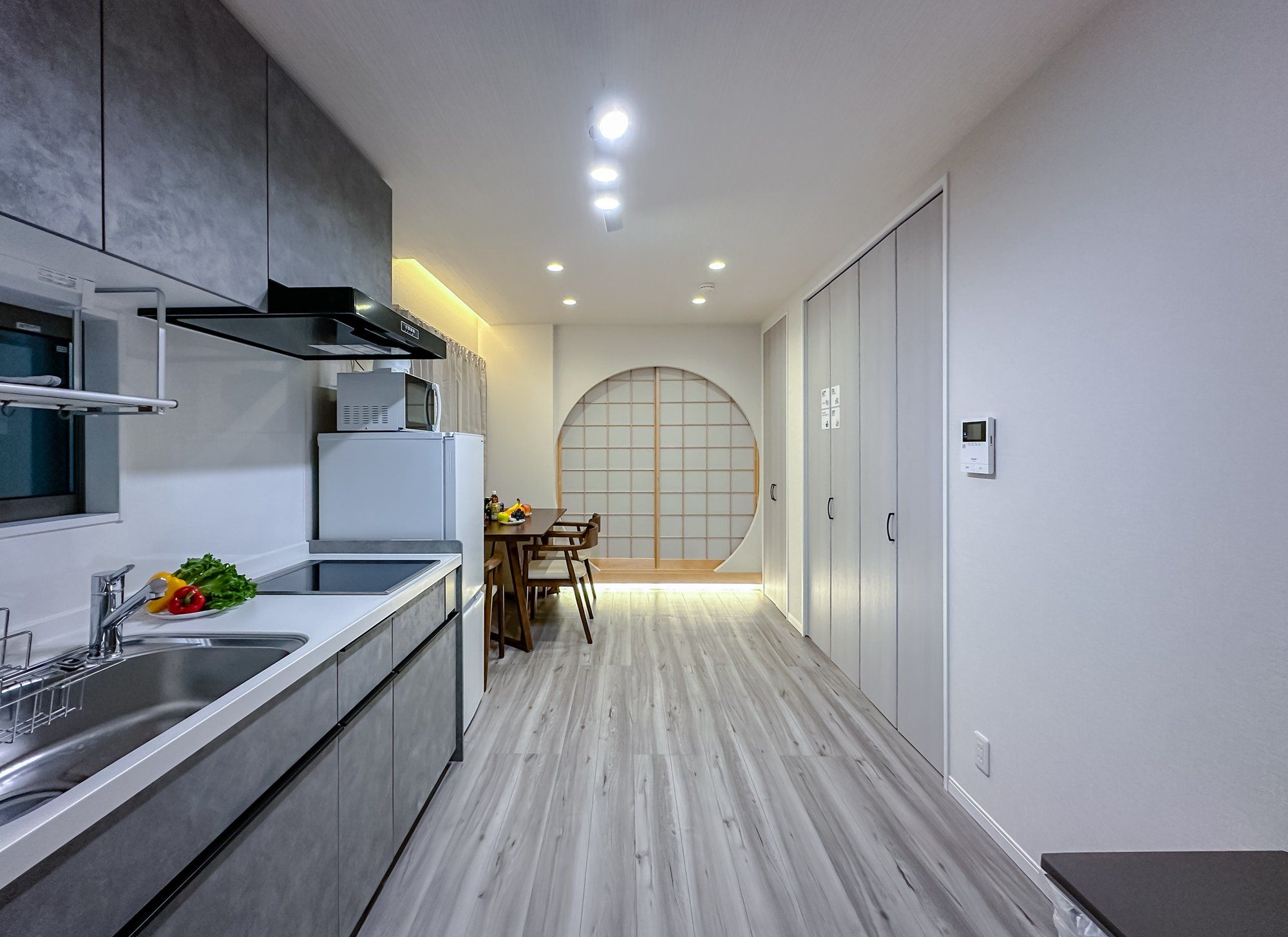 A modern kitchen with a built-in microwave, a refrigerator, and a sink. There is a dining area with a table and chairs.
