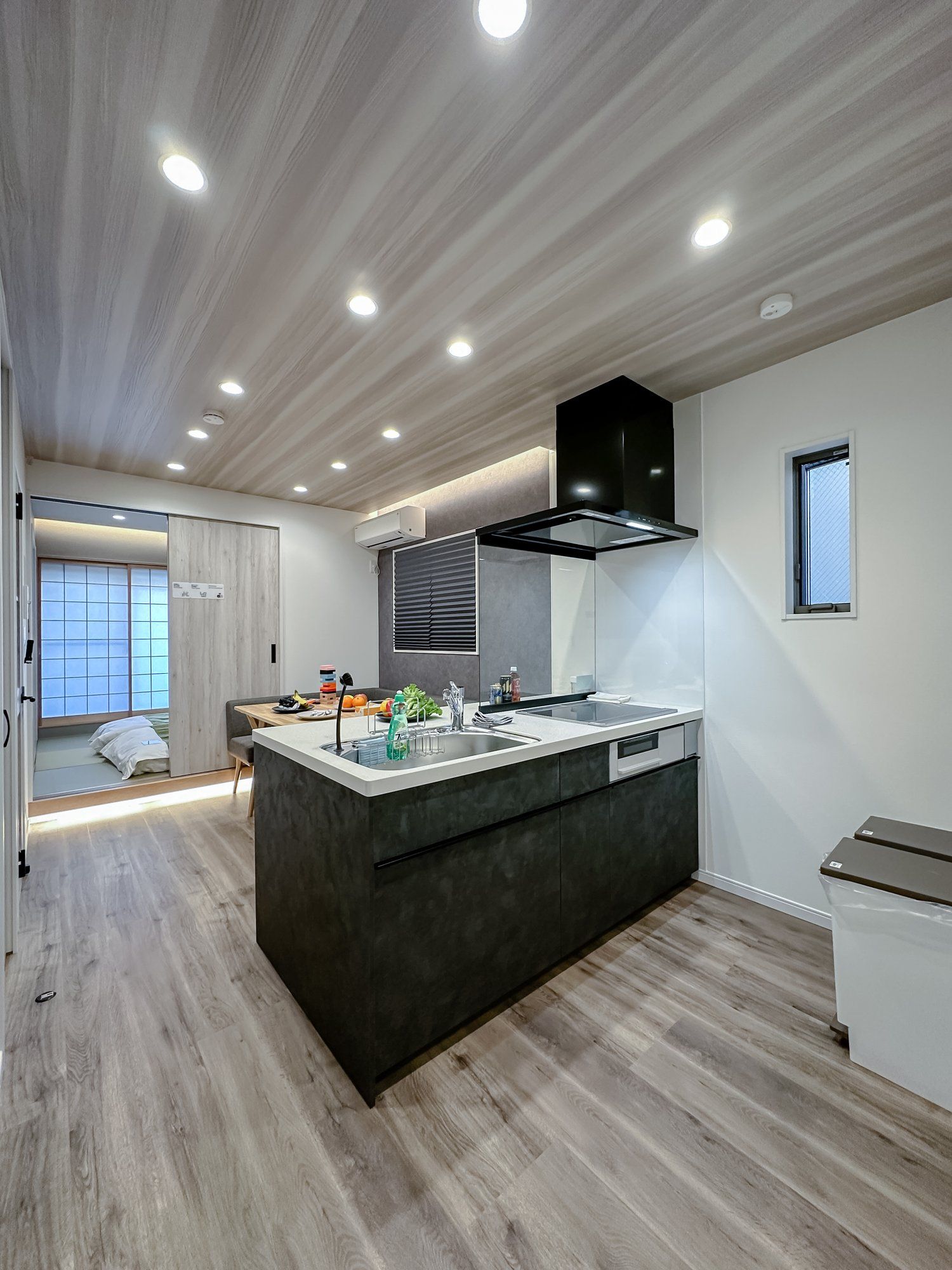 A modern kitchen with a central island, built-in oven, and a window with blinds.