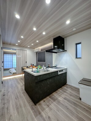 A modern kitchen with a central island, built-in oven, and a window with blinds. - HANASTAY KIWAMI (Osaka)