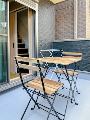 A patio area with a foldable table and chairs, a glass door entrance, and a brick wall. - HANASTAY KIWAMI (Osaka)