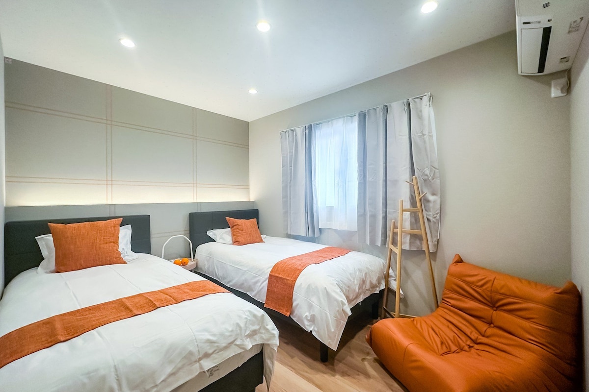 A hotel room with two beds, a wooden ladder, and a single orange chair.