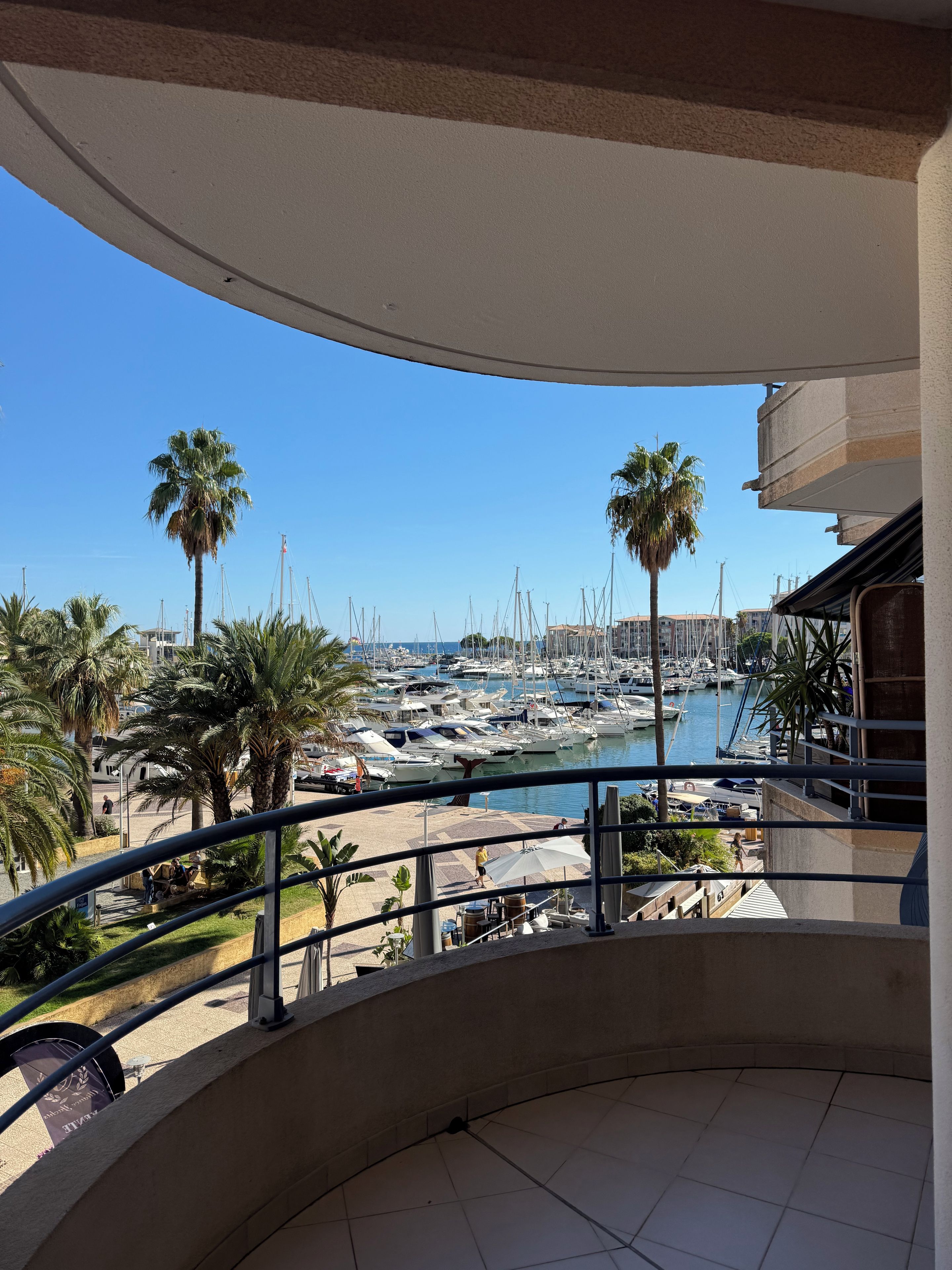 A balcony with a view of a marina, palm trees, and boats.