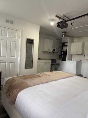 A bedroom with a bed, a ceiling fan, a microwave, and white cabinets. - Cozy Private Studio, 20 Minutes from Disney (Clermont)